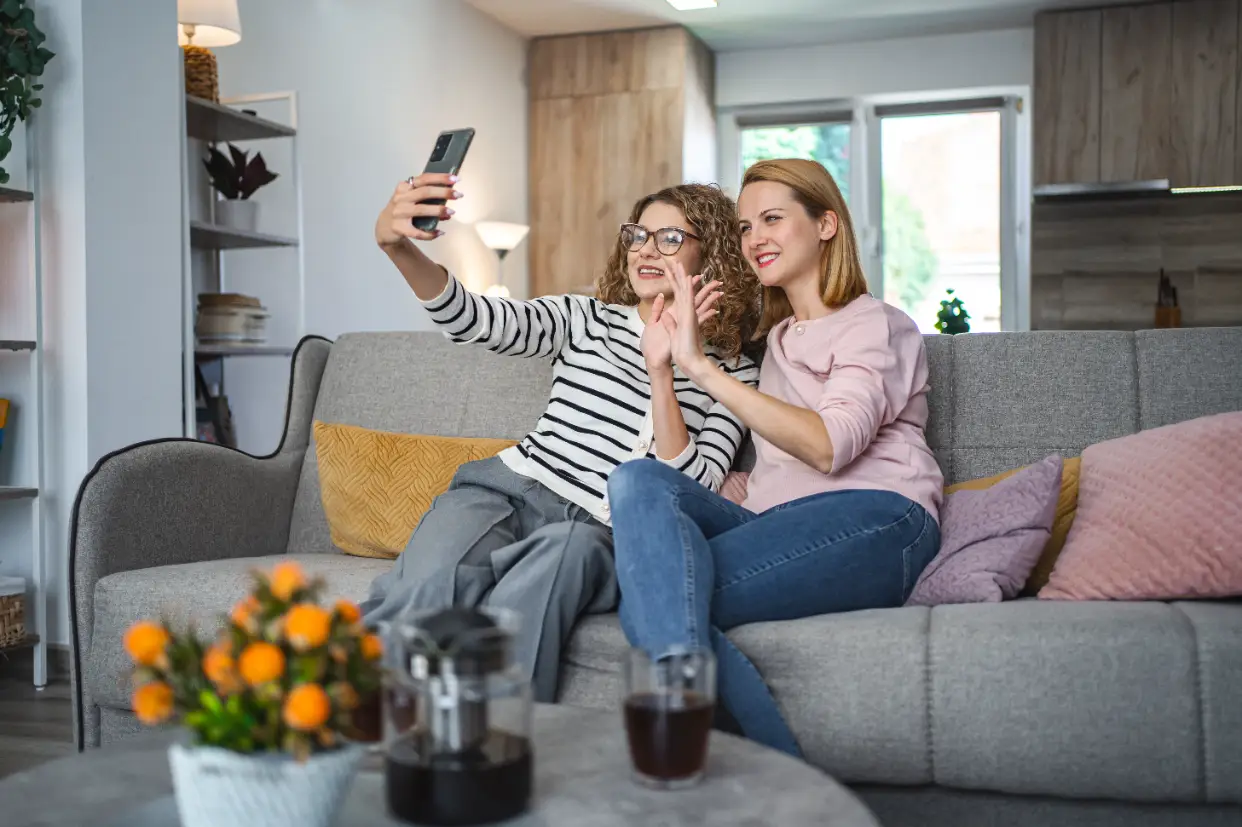 Paylaşımlı evin oturma odasında kanepede birlikte selfie çeken iki ev arkadaşı
